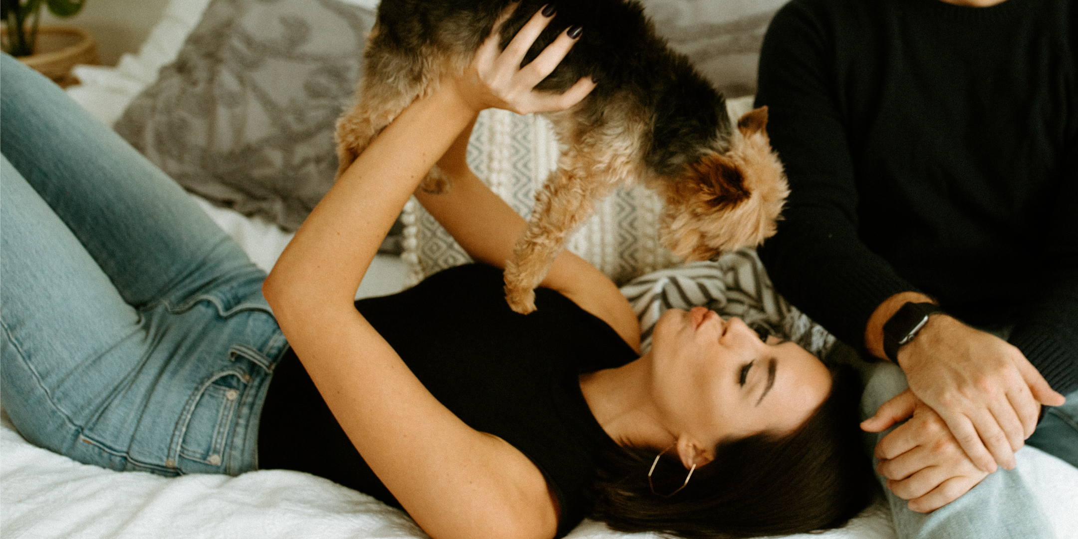 woman on bed holding her small dog above her head.